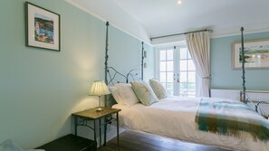 A bedroom with a bed, a bedside table with a lamp, a window with curtains, and a radiator. - Hafod Cae Maen -  a sea view that sleeps 8 guests  in 4 bedrooms (Penrhyndeudraeth)