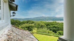A stone roofed balcony with a view of a lush green landscape and hills in the distance.