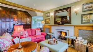 A cozy living room with a fireplace, wooden paneling, and a pink sofa.