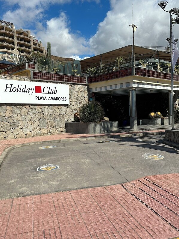 Welcome to the entrance of Holiday Club Playa Amadores, featuring a covered area with potted plants and a paved walkway.