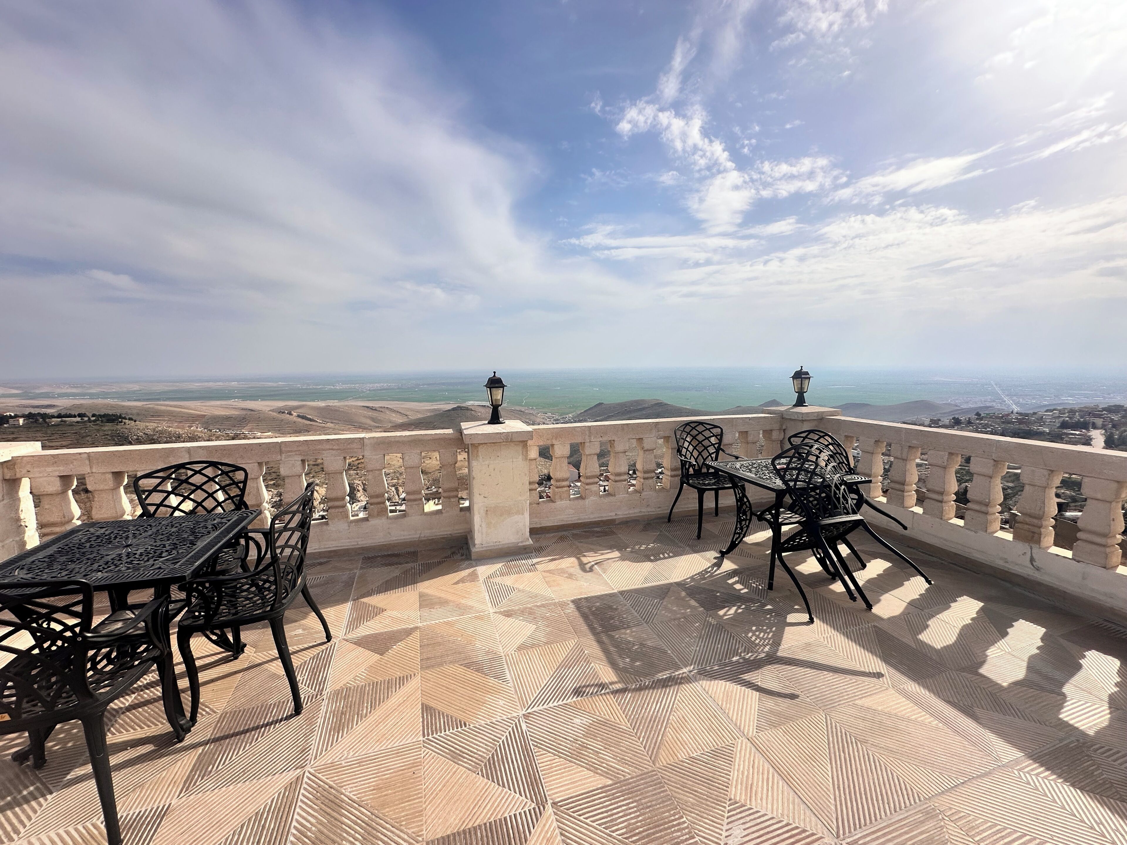 A terrace with a geometric patterned floor, two tables with chairs, and a view of the coastline.