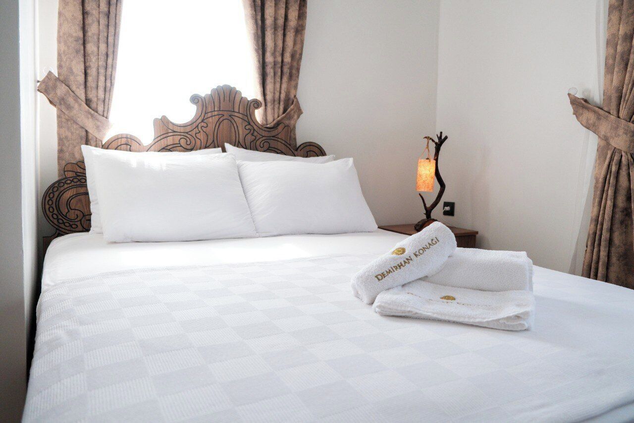 A neatly made bed with white linens and pillows, a decorative headboard, and a bedside lamp.