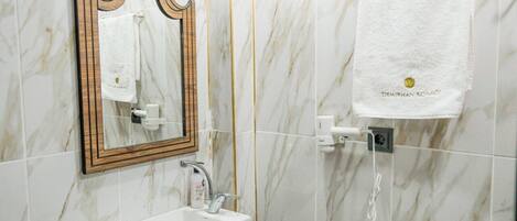 Un baño con pared de mármol, espejo con marco de madera, lavamanos blanco y un perchero con toalla blanca.