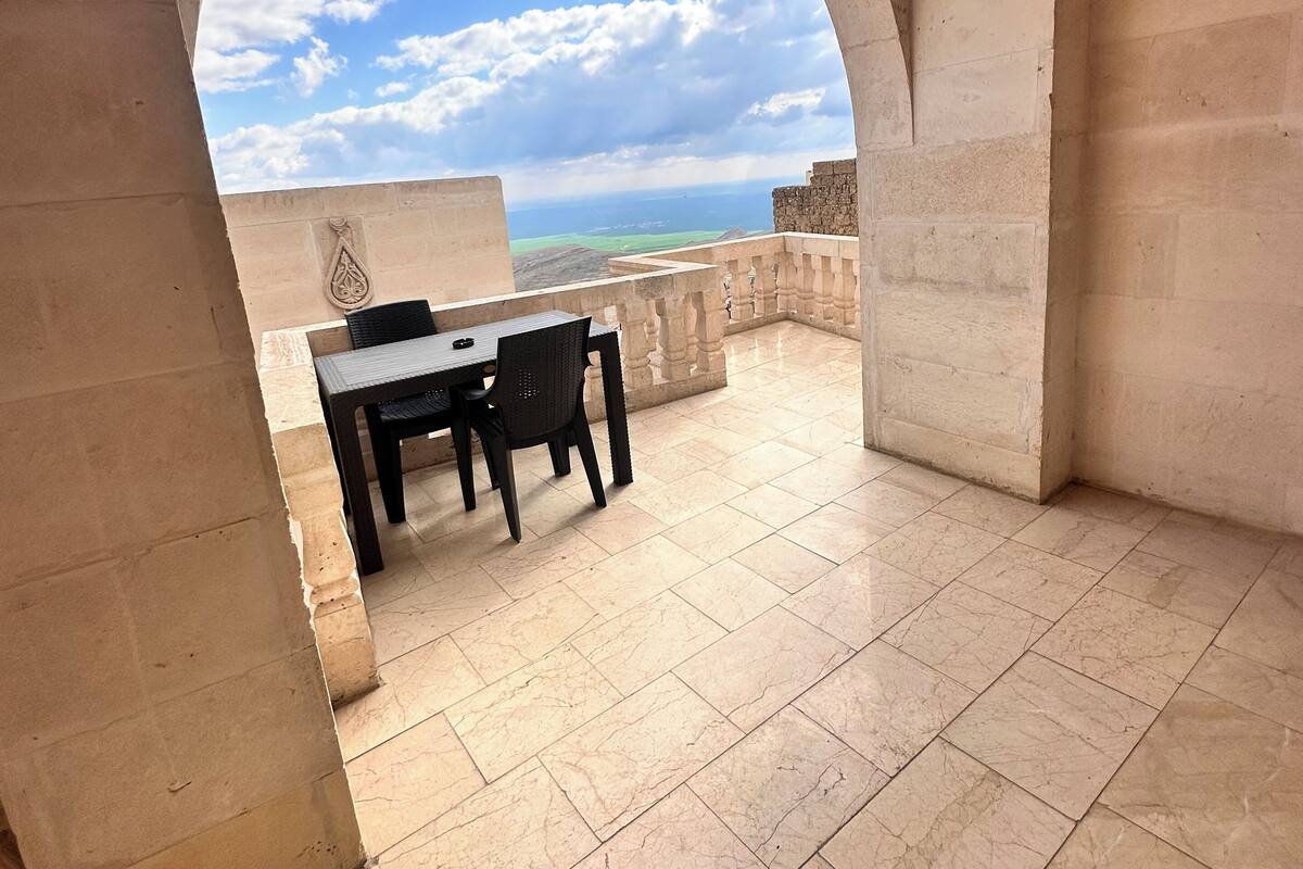 An open terrace with a table and chairs, a view of the sea, and a stone archway.