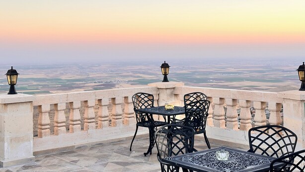A terrace with a table and chairs, overlooking a cityscape at sunset. - BABİ NEFES Demirhan Konağı (Mardin)