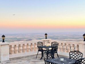 Une terrasse avec une table et des chaises, offrant une vue sur le paysage urbain au coucher du soleil.