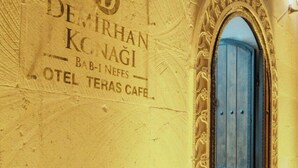 A wall with a sign for Demirhan Konagi and a door with a decorative arch. - BABİ NEFES Demirhan Konağı (Mardin)