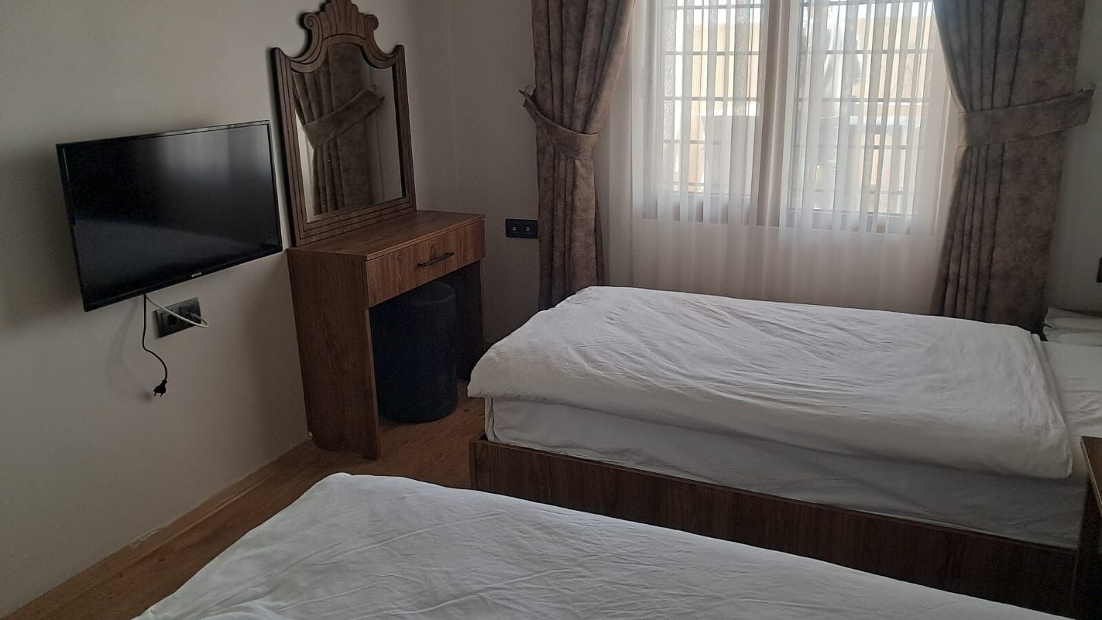 Un dormitorio con dos camas individuales, un aparador de madera, un televisor de pantalla plana y una ventana con cortinas.
