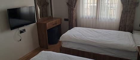 Un dormitorio con dos camas individuales, un aparador de madera, un televisor de pantalla plana y una ventana con cortinas.