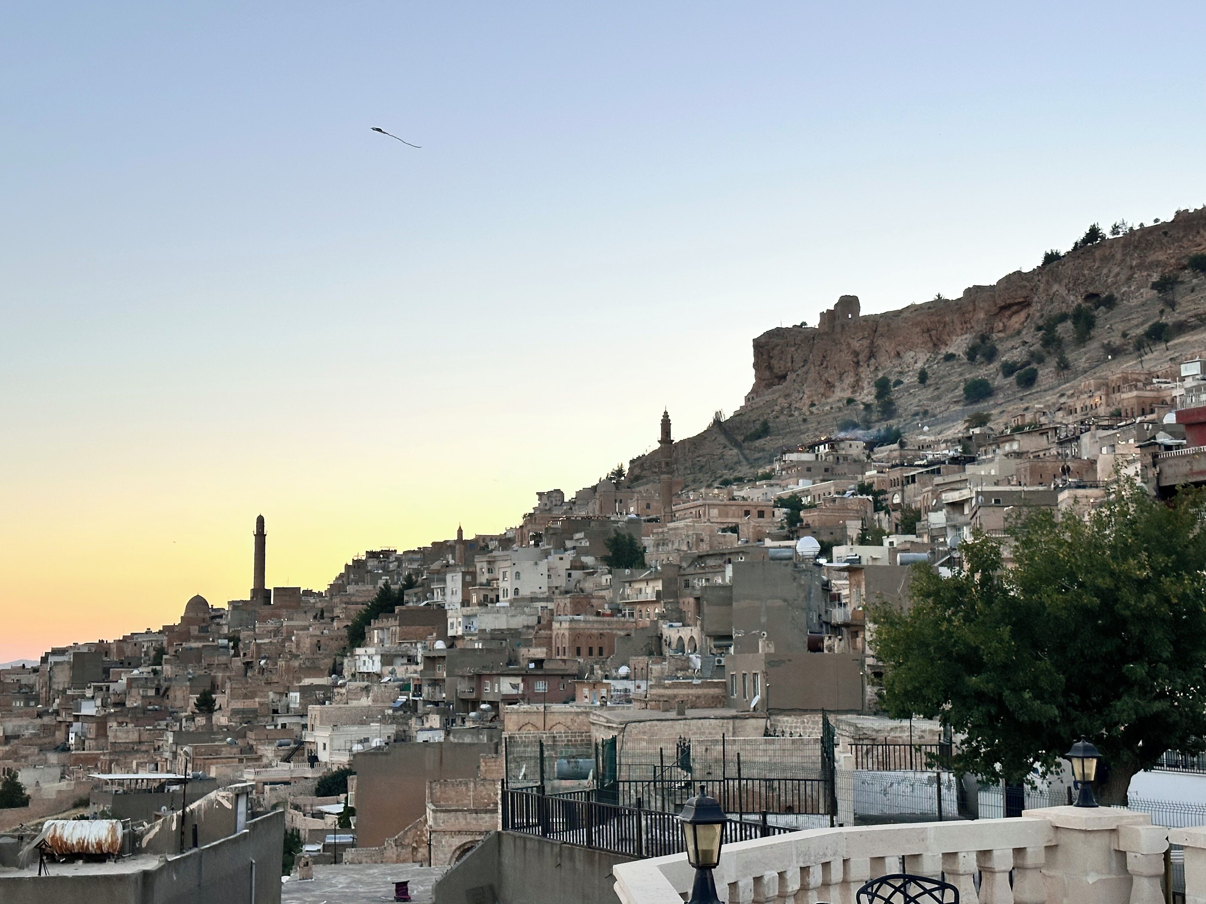 Un pueblo en una ladera densamente poblado con arquitectura tradicional, un minarete destacado y un cielo despejado.