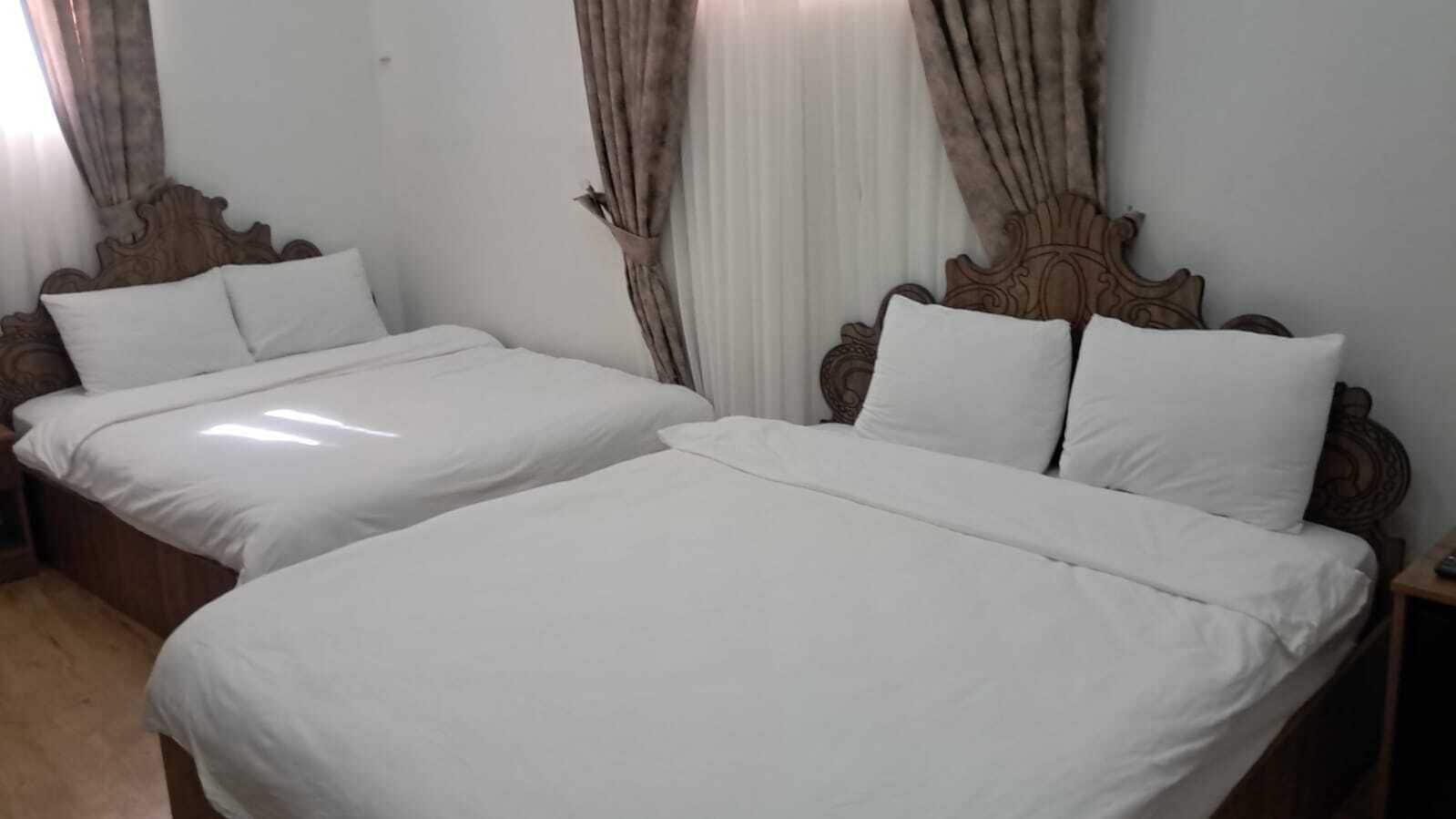 A hotel room with two single beds, wooden headboards, white bedding, and a nightstand with a lamp.