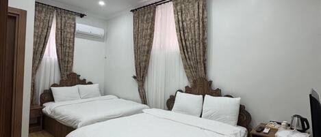 Habitación de hotel con dos camas, cabeceros de madera, ropa de cama blanca, un televisor de pantalla plana, cafetera y un equipo de aire acondicionado.