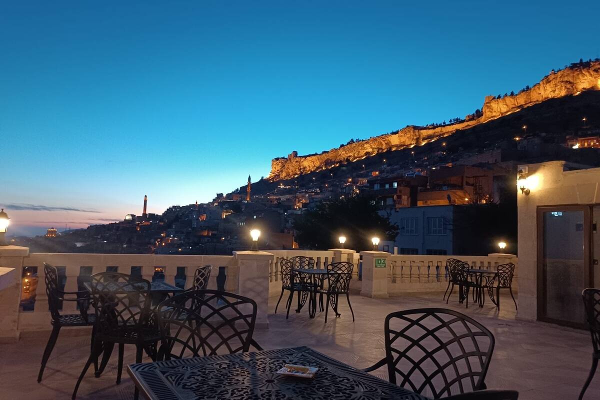 An outdoor seating area with tables and chairs, overlooking a cityscape with a prominent hill and buildings.