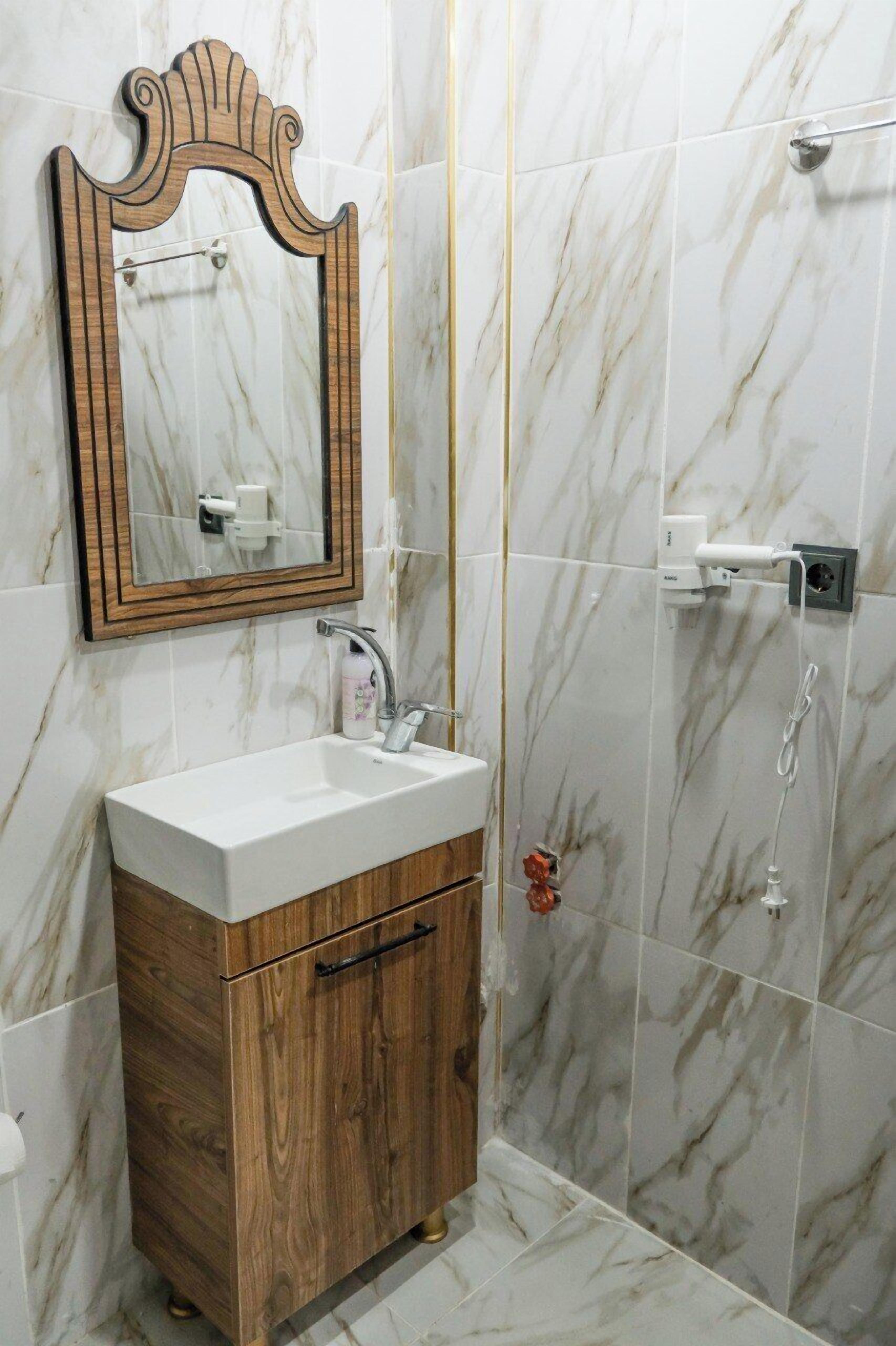 A bathroom with a wooden vanity, a marble-tiled shower area, and a wall-mounted mirror.
