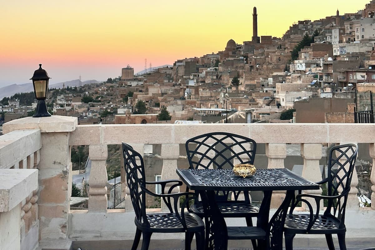 A terrace with a table and chairs overlooking a cityscape at sunset.