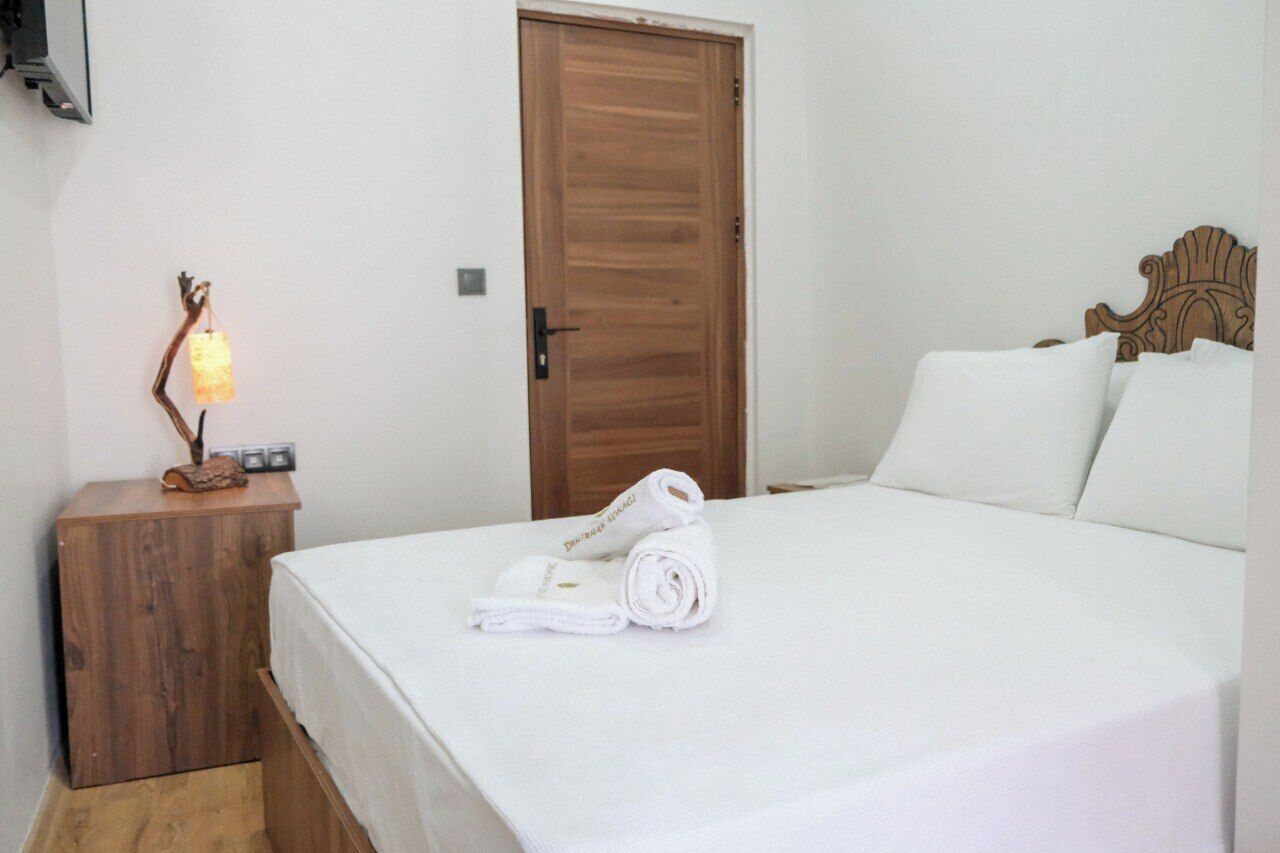 A neatly made bed with white linens, a wooden nightstand with a lamp, and a wooden door.