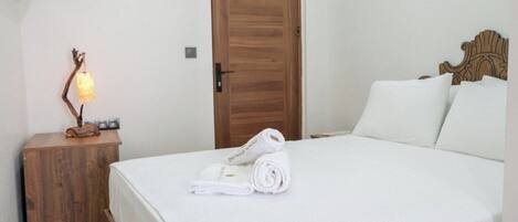 A neatly made bed with white linens, a wooden nightstand with a lamp, and a wooden door.