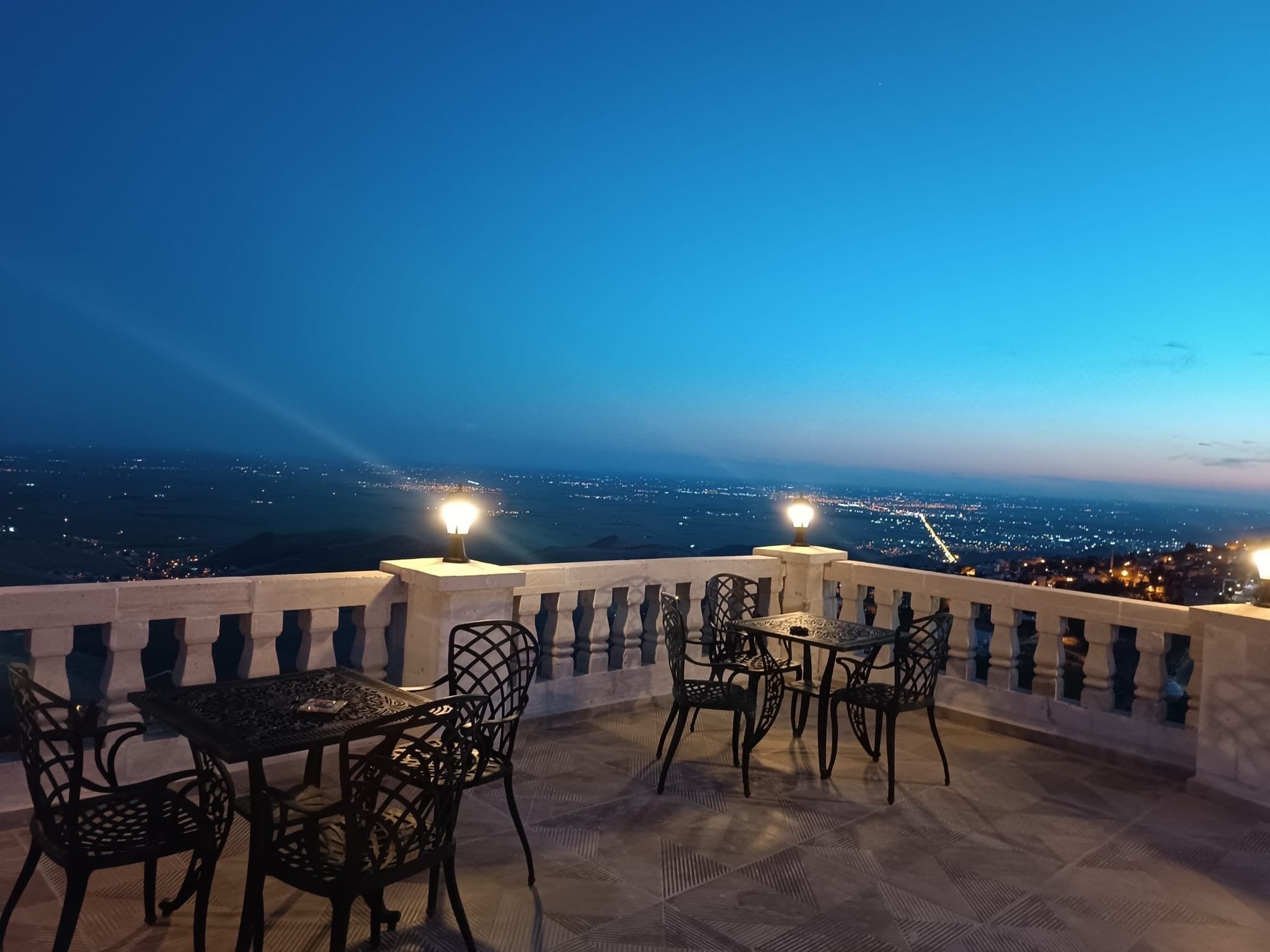 An outdoor terrace with a table and chairs, overlooking a cityscape at dusk.