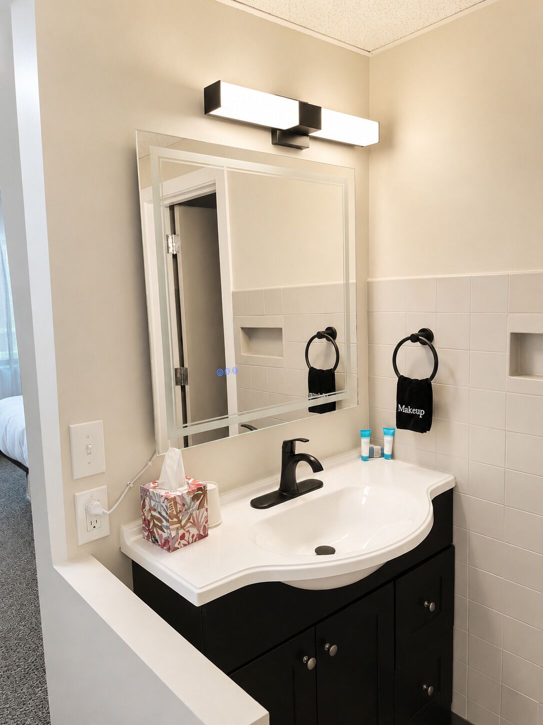 Un baño con un lavabo blanco, armarios negros, un espejo y un perchero para toallas.