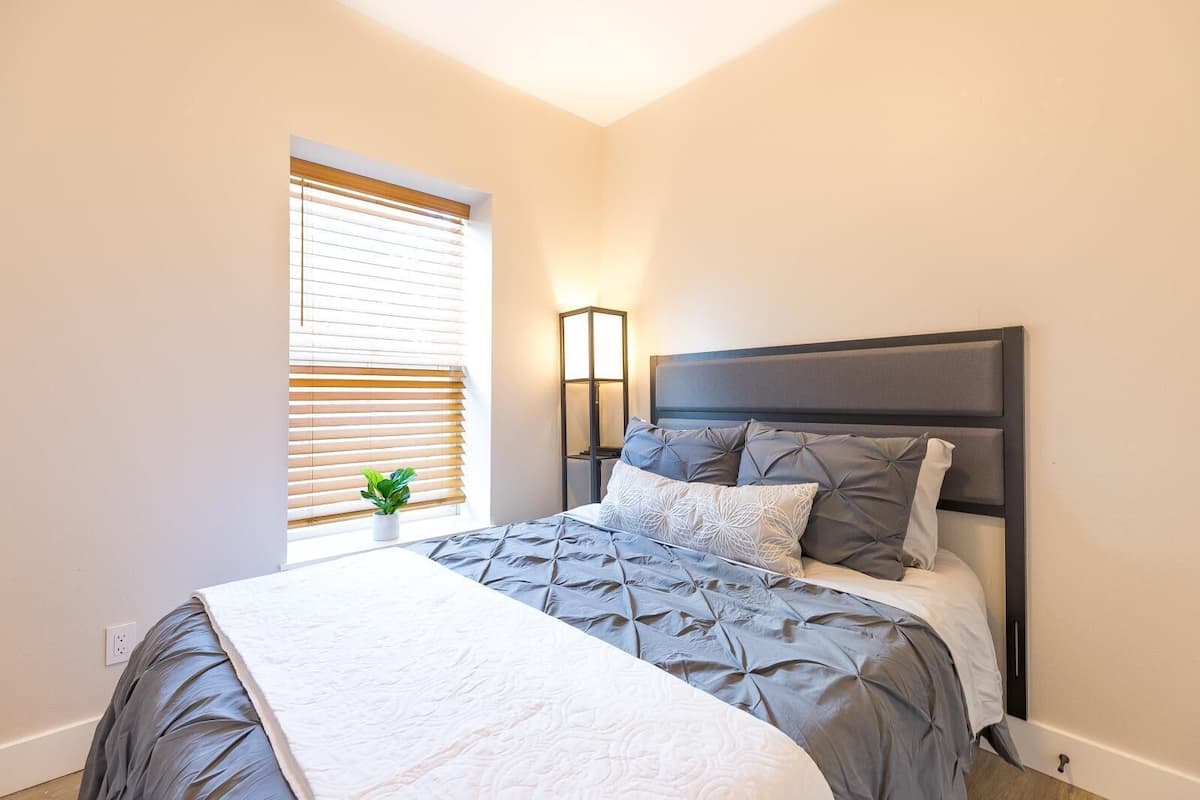 A bedroom with a bed, a bedside table, a lamp, and a window with blinds.