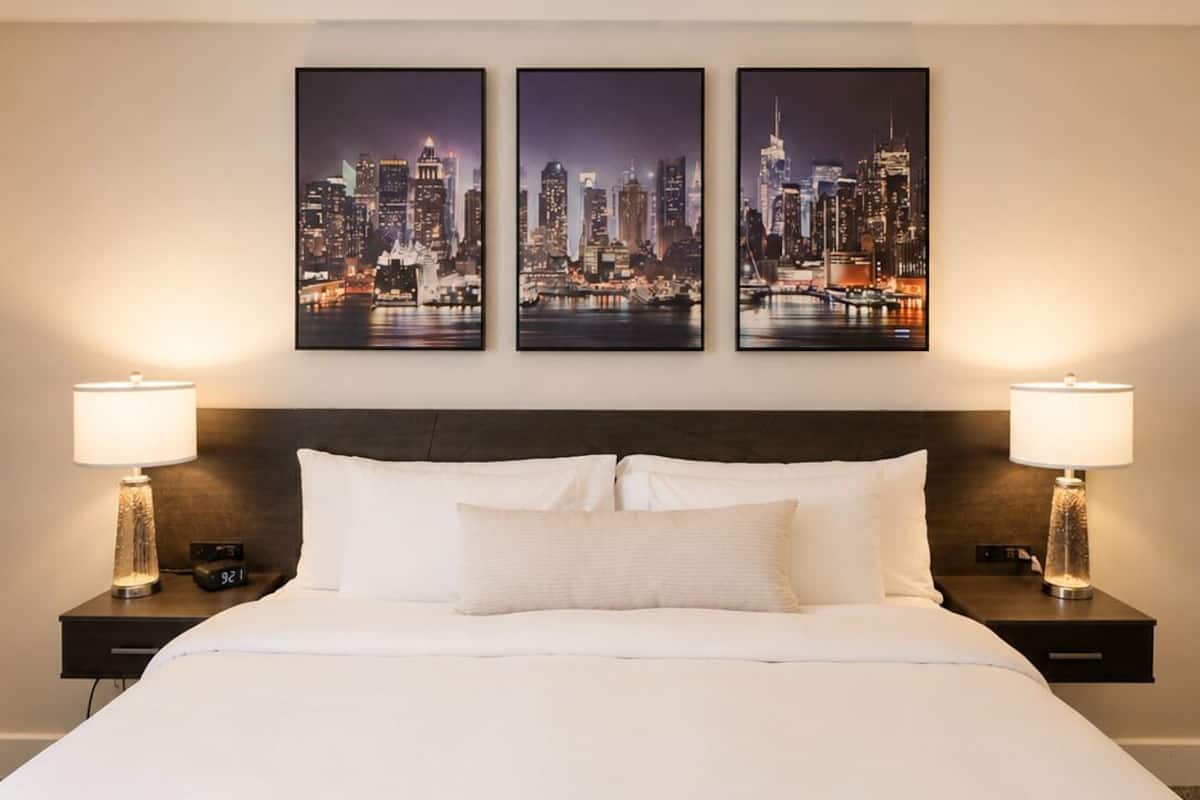 A hotel room with a large bed, two bedside tables with lamps, and three framed cityscape pictures on the wall.