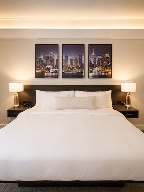 A hotel room with a large bed, two bedside tables with lamps, and three framed cityscape pictures on the wall. - Aisling Suites (Great Falls)