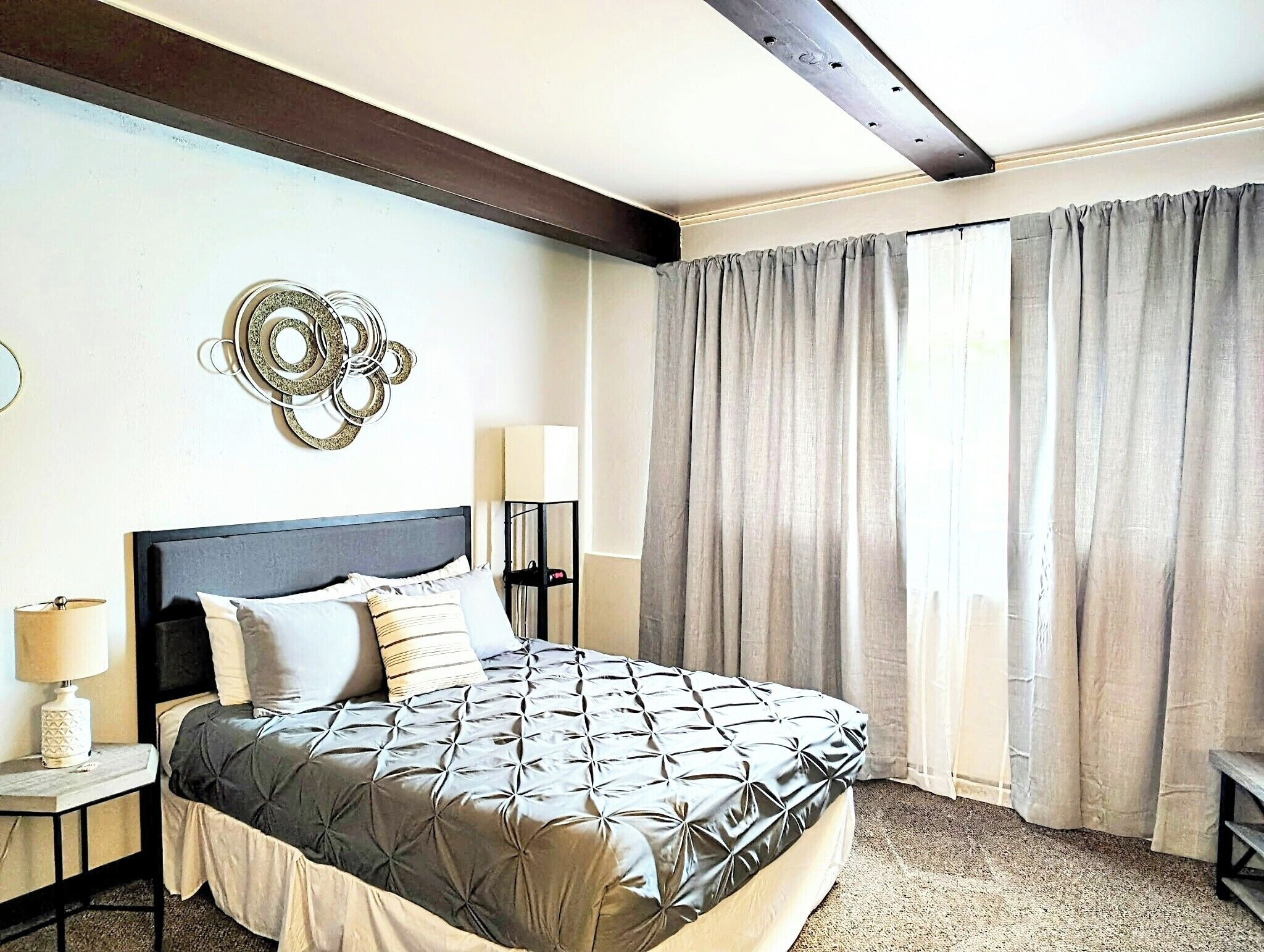 Habitación de hotel con cama, mesita de noche, lámpara, decoración en la pared y ventana con cortinas.