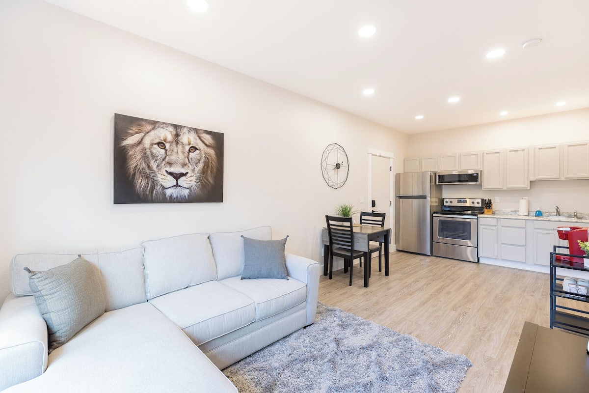 A modern living room with a white sofa, a grey rug, and a dining area with a table and chairs.