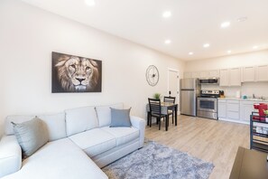 A modern living room with a white sofa, a grey rug, and a dining area with a table and chairs. - Aisling Suites (Great Falls)
