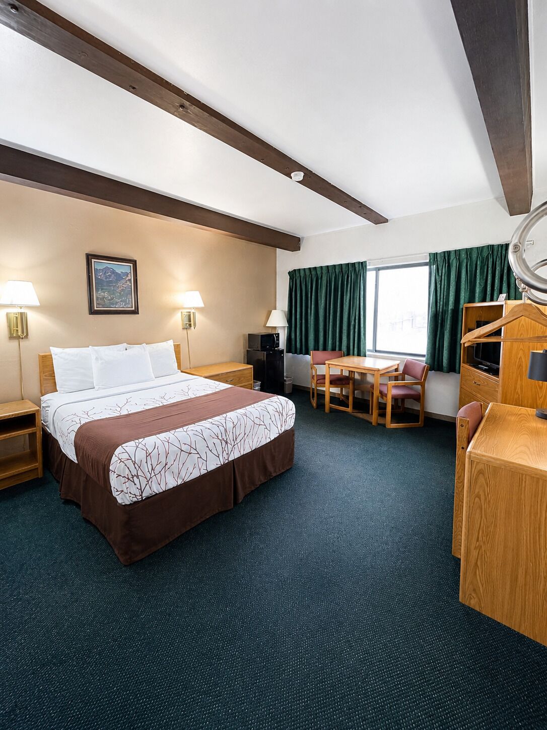 Ein Hotelzimmer mit Bett, Schreibtisch, Stuhl, Lampe und einem fensterbepflanzten Fenster.