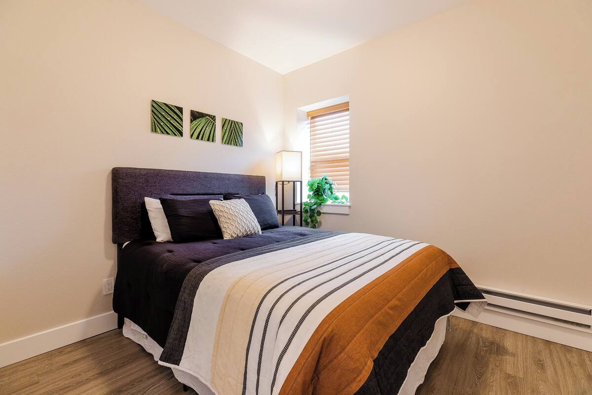 A bedroom with a bed, a bedside table, a lamp, and a window with blinds.