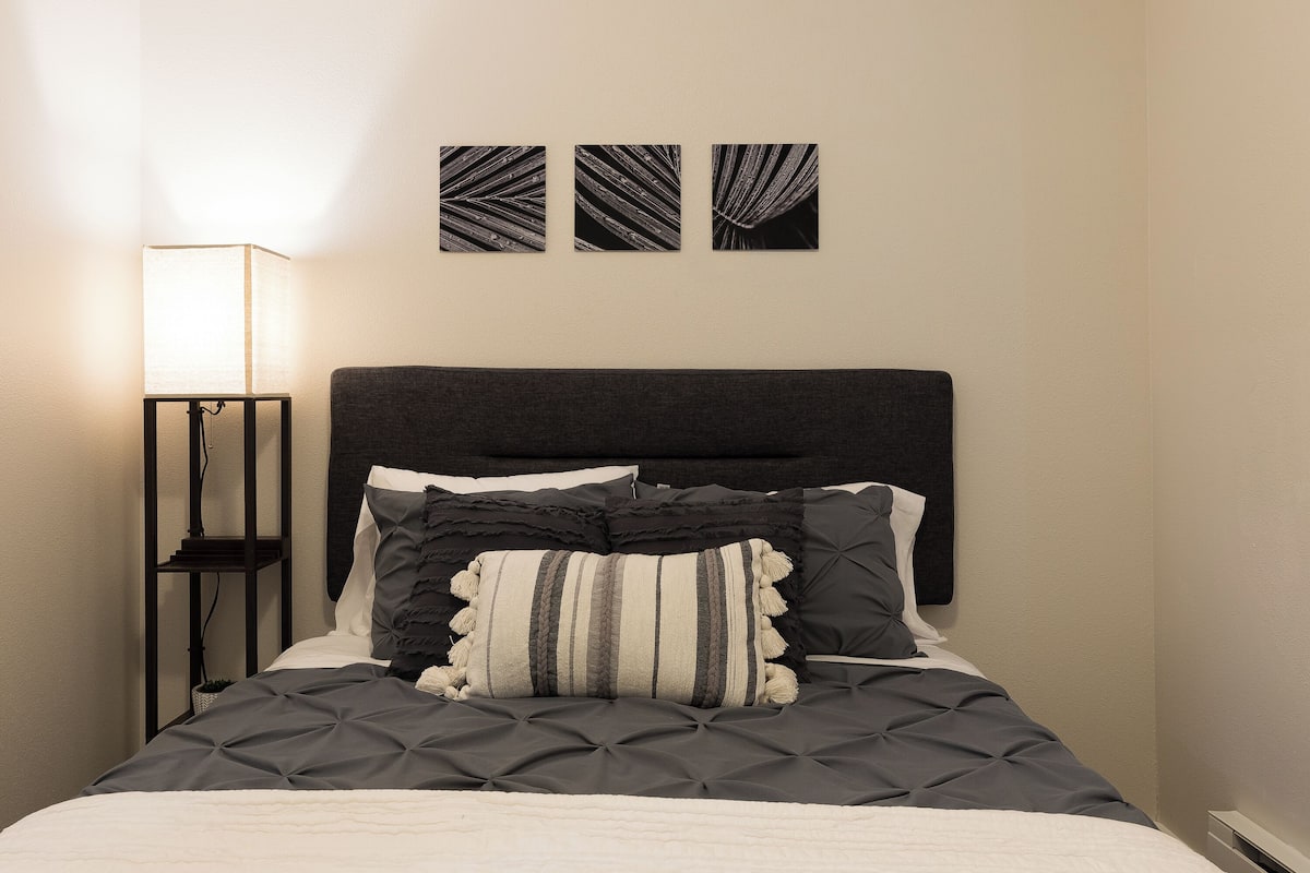 A neatly made bed with a dark headboard, a bedside lamp, and three framed pictures on the wall.