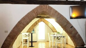 An arched brick ceiling in a room with a tiled floor, white furniture, and a television mounted on the wall. - The arches in the heart of Siena (Siena)