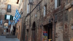 A narrow street with brick buildings, outdoor seating, and blue and white patterned flags. - The arches in the heart of Siena (Siena)