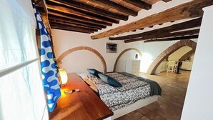 A bedroom with a wooden desk, a bed with patterned bedding, and a view of an adjacent room through an arched doorway. - The arches in the heart of Siena (Siena)