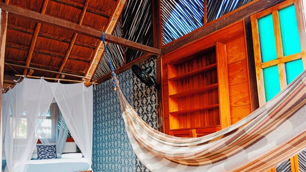 Una habitación con una cama bajo un dosel, una hamaca, estantes de madera y papel tapiz estampado.