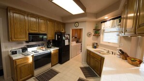 Une cuisine avec des meubles de rangement en bois, une cuisinière, un four à micro-ondes, un réfrigérateur et une fenêtre avec des rideaux.