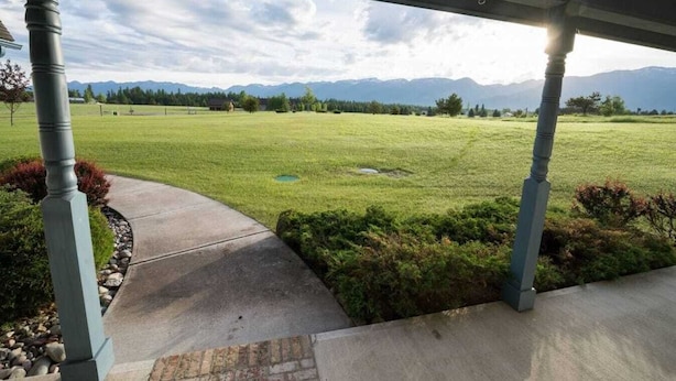 Un espace extérieur abrité, avec un chemin en béton menant à un champ herbeux et des montagnes en arrière-plan.