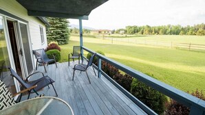 Une terrasse couverte, aménagée avec du mobilier d’extérieur, offrant une vue sur un champ verdoyant et un bâtiment situé au loin.
