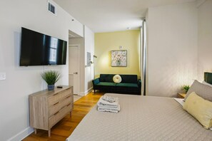 A bedroom with a large bed, a television mounted on the wall, a green sofa, and a painting on the wall.