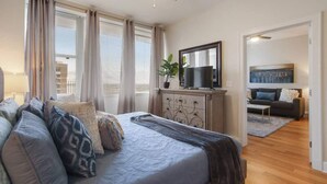Camera da letto moderna con un letto grande, una cassettiera, una TV e vista sulla città dalle finestre.