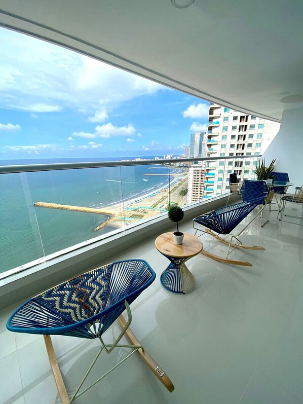A balcony with a view of the sea and a cityscape, furnished with blue chairs and a small table. - U-GO Edificio Palmetto Eliptic Cartagena (Cartagena)