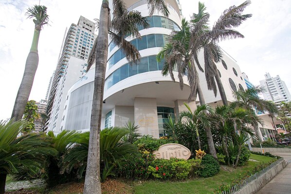 Un edificio moderno con fachada curva, rodeado de palmeras y un jardín bien cuidado.