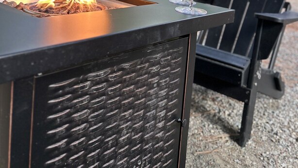 A fire feature with a glass of red wine on a metal table, surrounded by outdoor chairs. - Cozy Pines Cabin (Ronald)