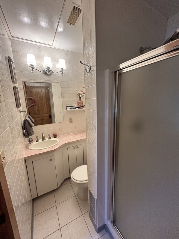 A bathroom with a sink, toilet, and shower. There is a mirror above the sink and a towel rack on the wall. - Cozy Pines Cabin (Ronald)