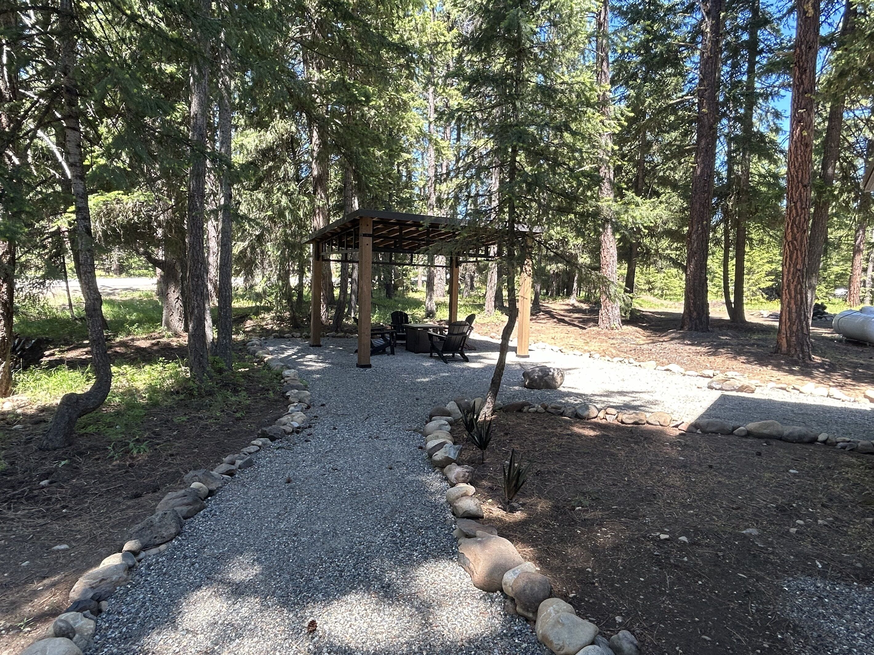 A covered outdoor seating area with a gravel path leading to it, surrounded by trees.
