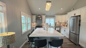 Una cocina moderna con una isla central, taburetes de bar, una lámpara colgante y un horno empotrado.