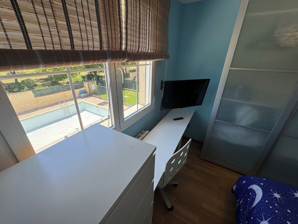 Un dormitorio con escritorio, televisor y ventana con vistas a una piscina.