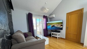 A living room with a grey sofa, a coffee table, a TV on a stand, and a wooden door. - Casa Ribera del Pisuerga - Piscina Privada a 10 Minutos del Centro de Valladolid (Arroyo de la Encomienda)