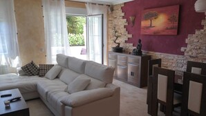 A living room with a beige sofa, a coffee table, and a TV. There is a stone wall with a painting of a tree and a statue. - Casa Ribera del Pisuerga - Piscina Privada a 10 Minutos del Centro de Valladolid (Arroyo de la Encomienda)